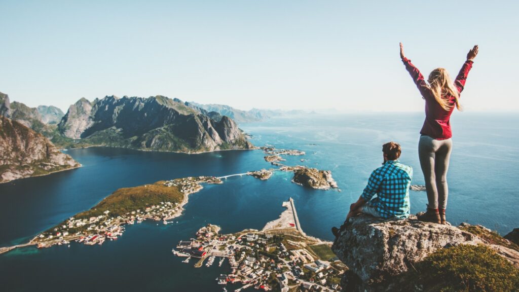 Couple family traveling together on cliff edge in Norway man and woman lifestyle concept summer vacations outdoor aerial view Lofoten islands Reinebringen mountain top