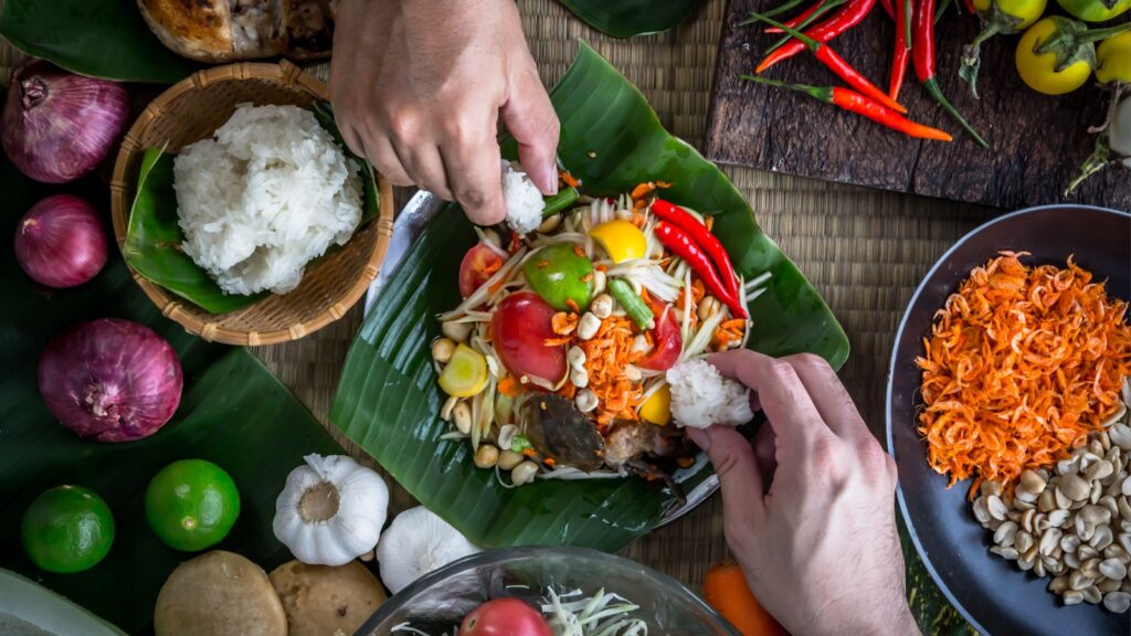 Hands holding sticky rice to eat with Thai papaya salad or what we call " Somtum " in Thai with ingredients. The famous local Thai street food with hot and spicy dish. Food stylish photography concept