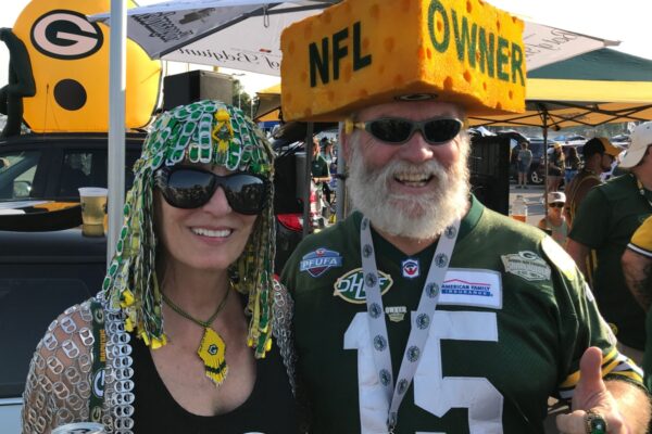 Green Bay, Wisconsin. August 9th, 2018. Packer fans during at tailgate party at Lambeau Field. The man wears a cheesehead that says NFL Owner. The Packers are the only publicly owned NFL team.