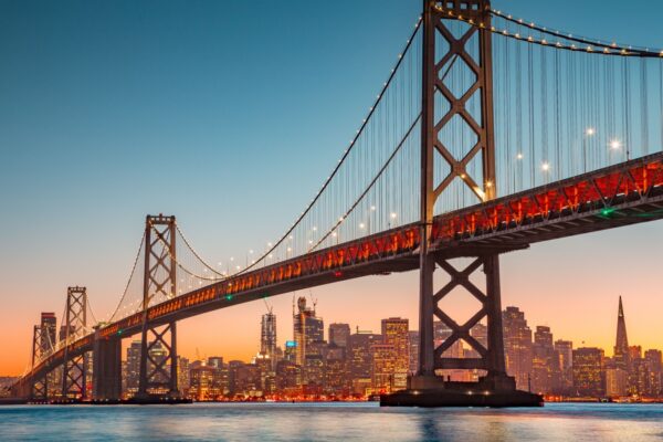 Classic panoramic view of San Francisco skyline with famous Oakland Bay Bridge illuminated in beautiful golden evening light at sunset in summer, San Francisco Bay Area, California, USA