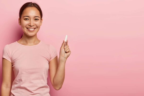 Pretty dark haired female with Asian appearance, holds cotton tampon, cares about hygiene during menstruation, has happy look, dressed in casual outfit. Women, health care, wellbeing concept