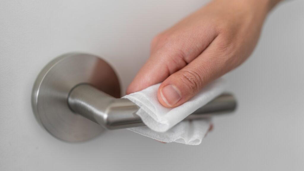 Coronavirus COVID-19 Prevention cleaning woman wiping doorknob with antibacterial disinfecting wipe for killing corona virus on touching surfaces or touching public bathroom handle with tissue.