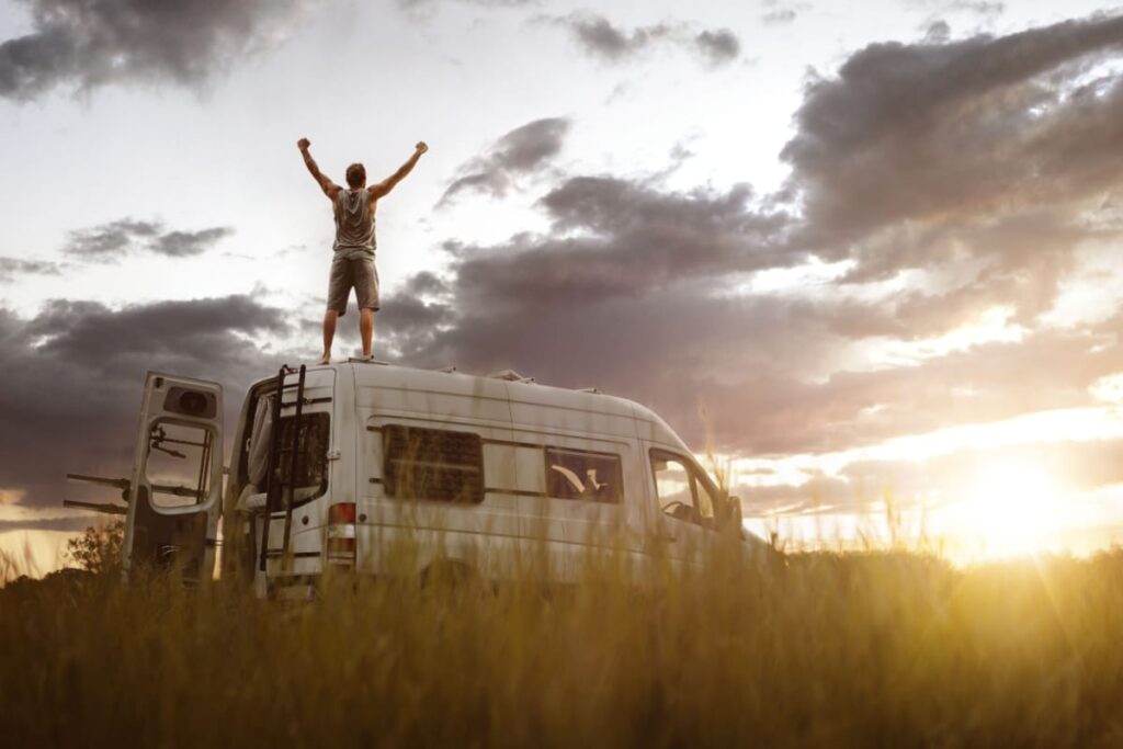 Man with raised arms on top of his camper van