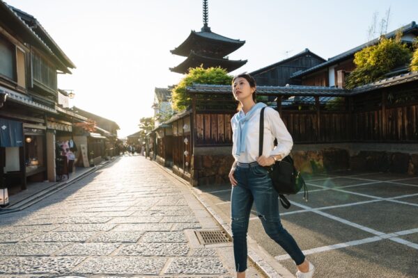 low angle and full length asian girl backpacker is gazing into the distance while wandering around at Yasaka dori near Hokanji Temple in Kyoto, japan at dusk.
