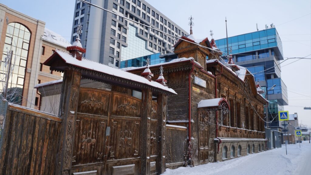Chelyabinsk, Russia – 1 January 2023: old wooden manor with a gate next to a new building.