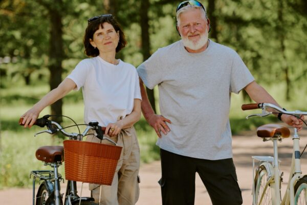 Senior couple holding their retro style bikes while smiling and posing for photo in park