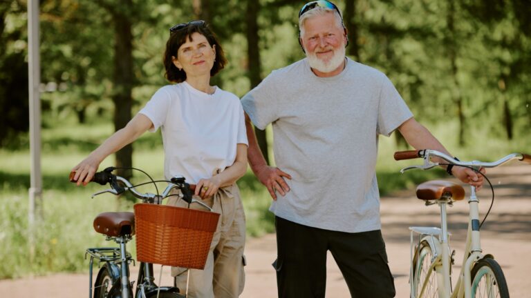 Senior couple holding their retro style bikes while smiling and posing for photo in park