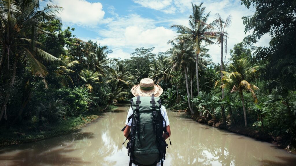 Traveling woman with backpack and straw hat looking at tropical river at sunny day