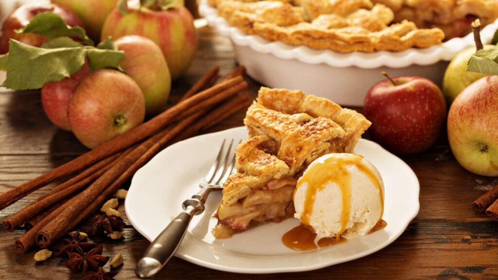 Apple pie and ice cream on a white plate with apples in the background