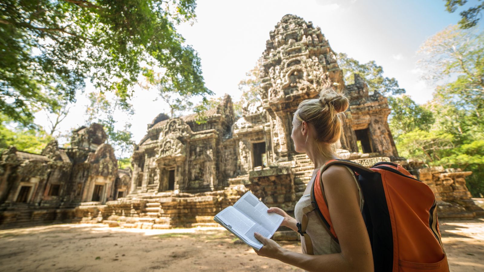 A woman holding an open book looking at an ancient structure