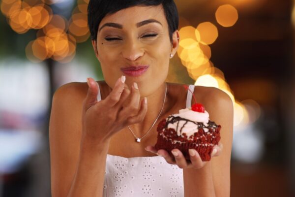 Smiling black female eating fancy cupcake in outdoor setting with bokeh lights