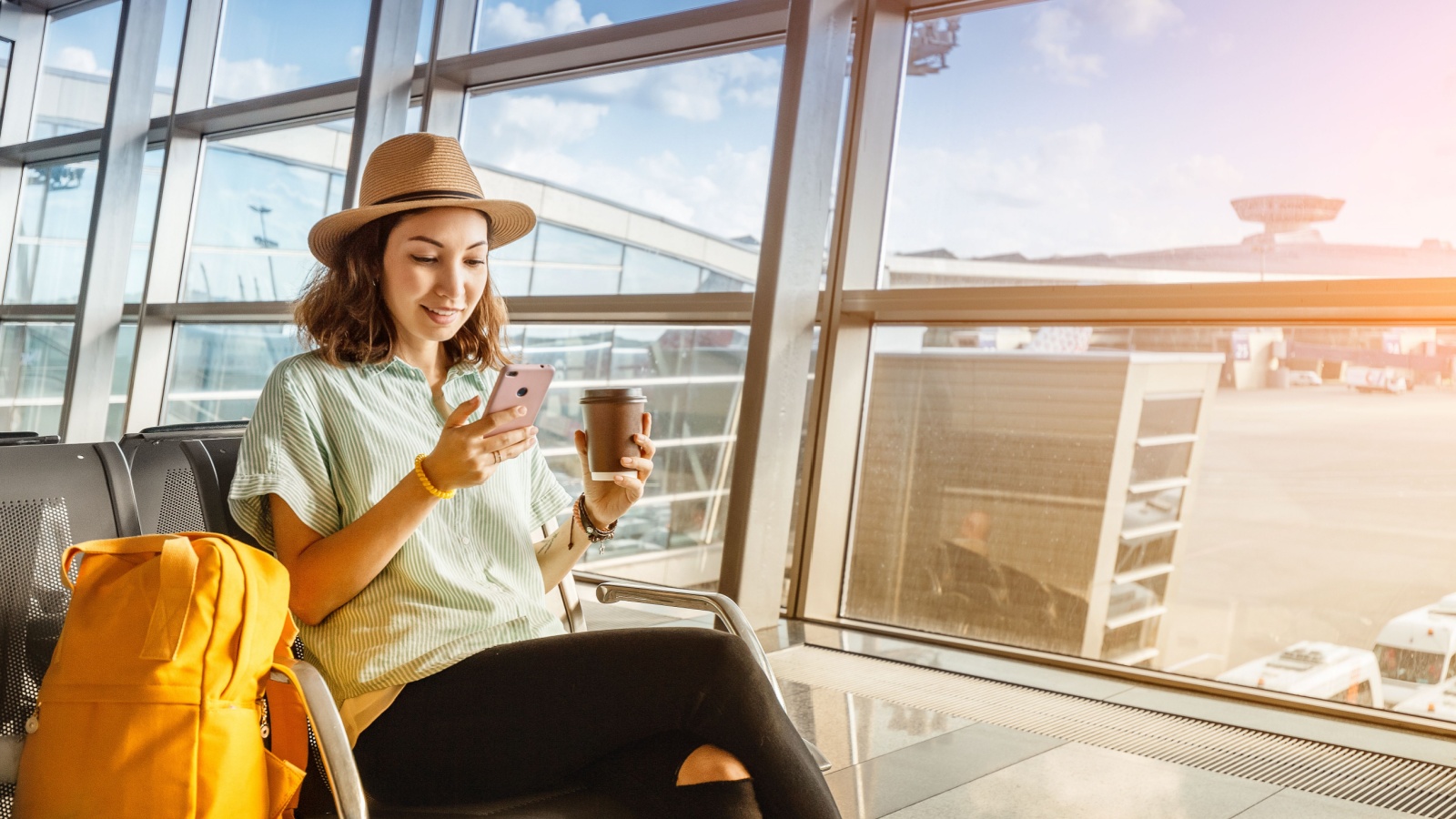 Asian girl waiting for departure at the airport on your vacation. Uses a smartphone and drinks coffee