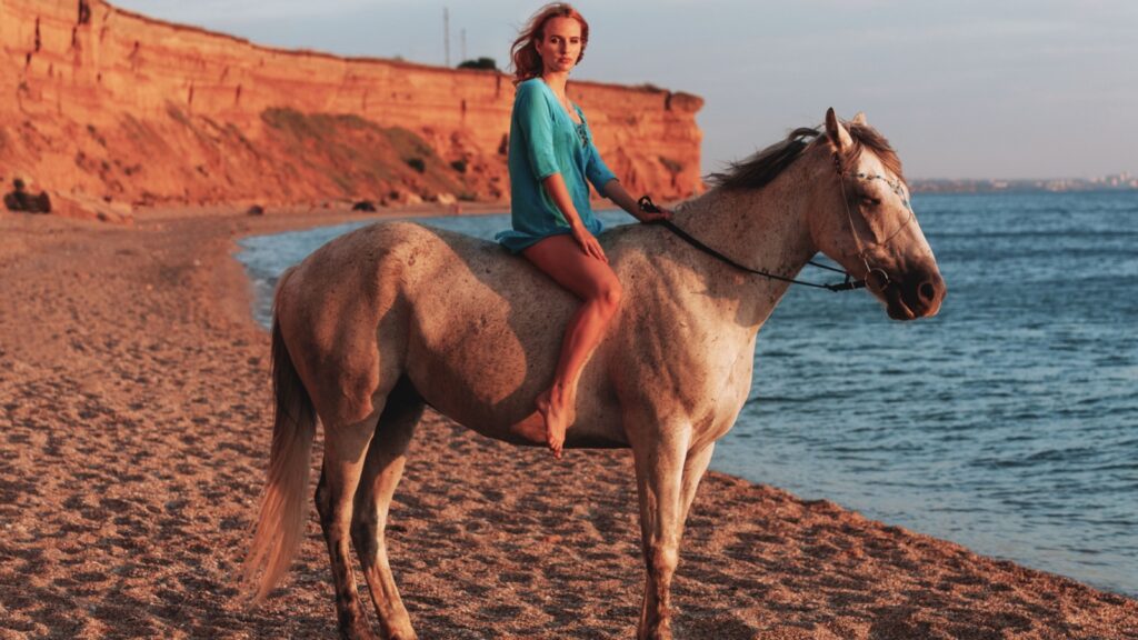 beautiful young girl riding a horse walking along the sandy beach at sunset time
