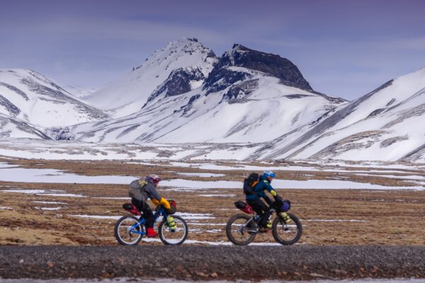 Two people cycle through a snow covered, mountainous landscape in Western Iceland