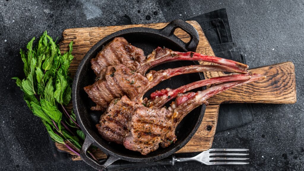 BBq Grilled lamb mutton chops steaks in a pan. Black background. Top view