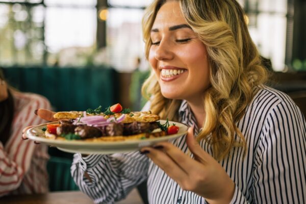 Beautiful blonde woman happy to eat grilled meat in a restaurant with her friends.