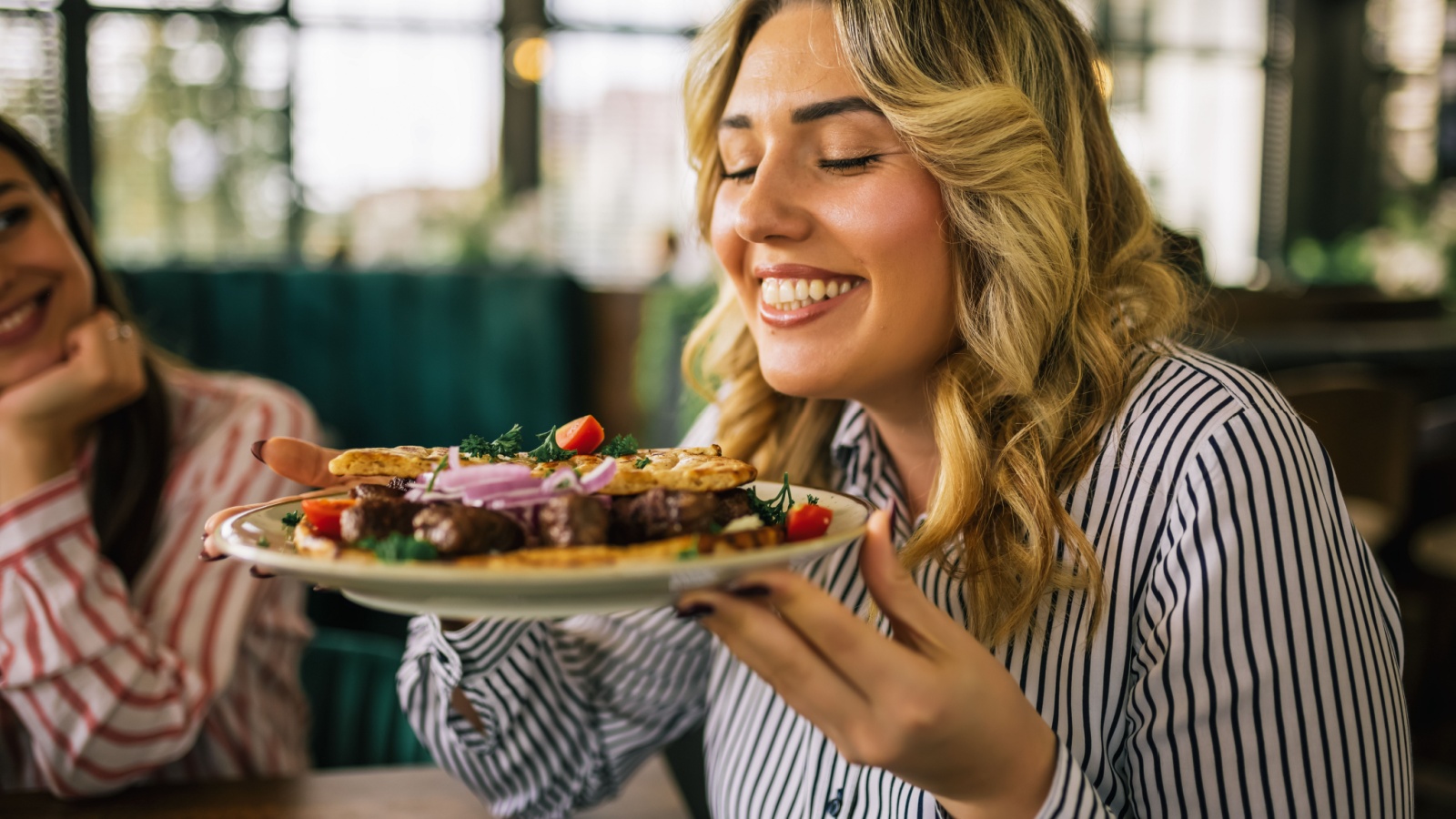 Beautiful blonde woman happy to eat grilled meat in a restaurant with her friends.