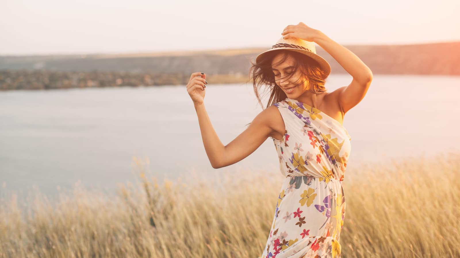 Beauty young girl outdoors enjoying nature. Fashion young woman in floral dress and stylish hat in meadow with copy space