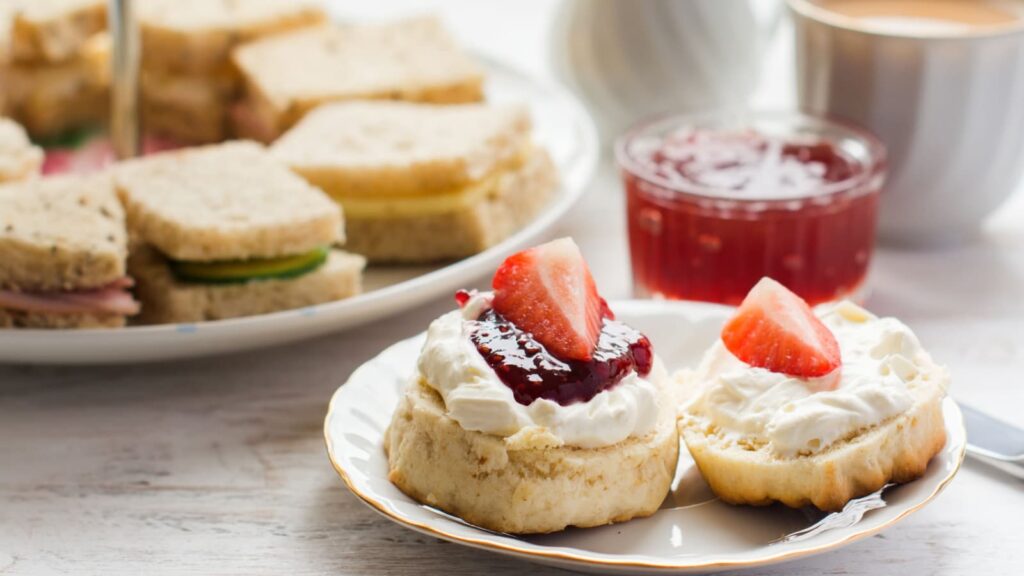 Traditional English afternoon tea: scones with clotted cream and jam, strawberries, with various sandwiches on the background, selective focus