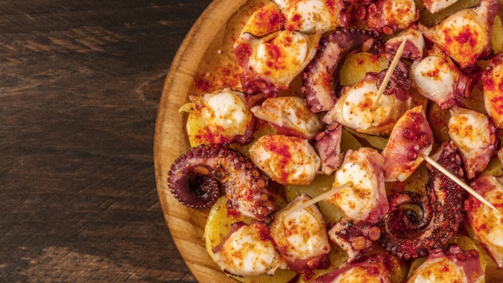 A closeup photo of pulpo a la gallega, an octopus with boiled potatoes, typical Spanish Galician dish, on a traditional wooden plate, with copy space