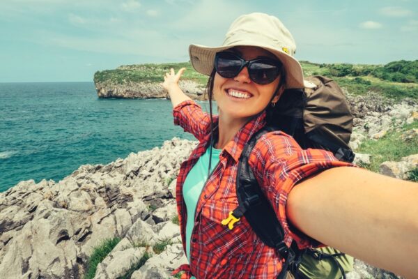 Happy woman backpacker traveler take a selfie photo on amazing ocean coast