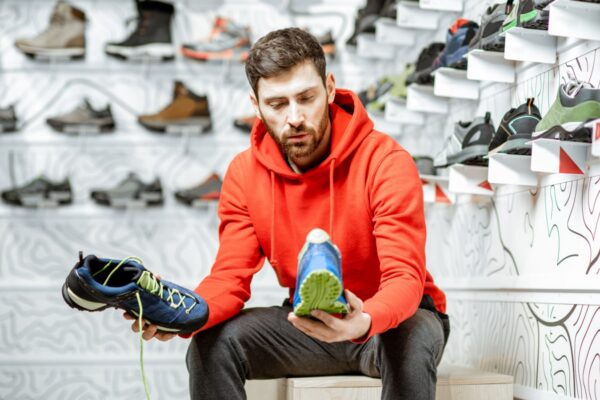 Man choosing trail shoes for hiking sitting in the fitting room of the modern sports shop