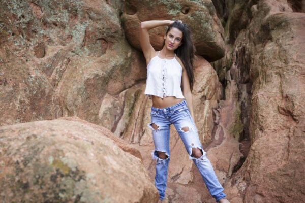 Sassy young model in ripped jeans and white t-shirt posing with one arm over her head