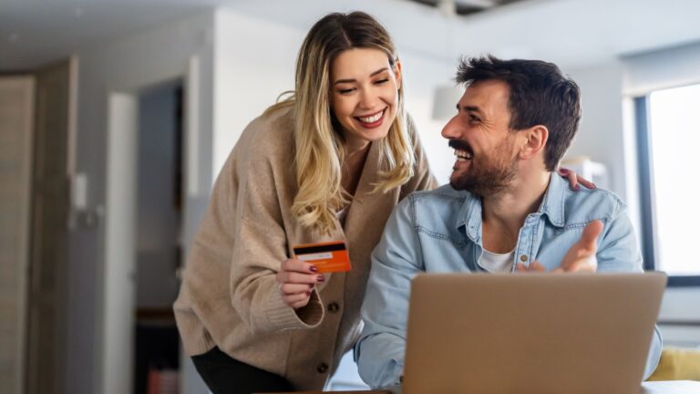 Cheerful young couple using laptop and smiling while shopping online at home