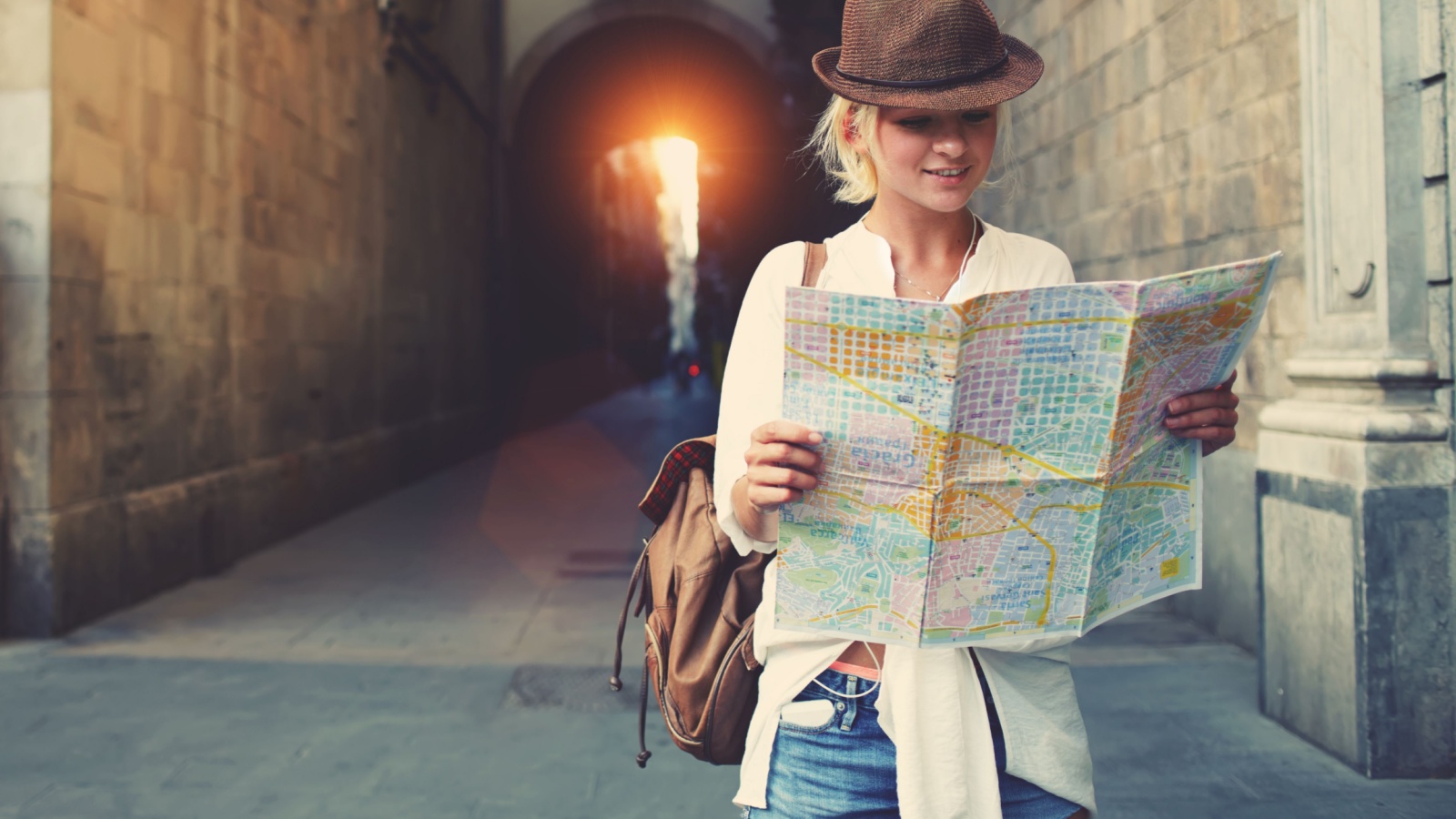 Cheerful woman wanderer with trendy look searching direction on location map while traveling abroad in summer, happy female tourist searching road to hotel on atlas in a foreign city during vacation
