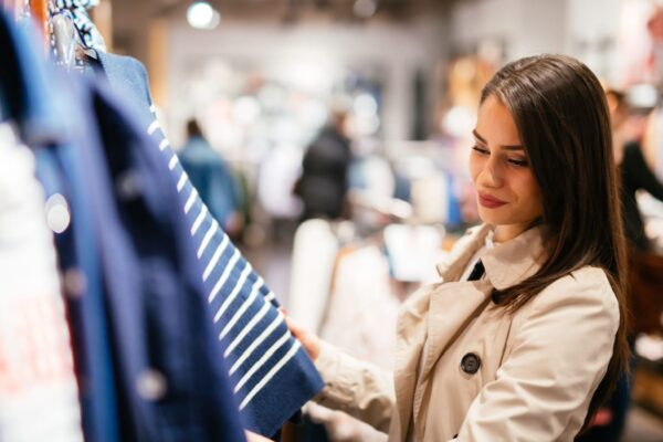 A woman shopping for clothes in a retail store. She admires a blue and white stripped top on the hanger.