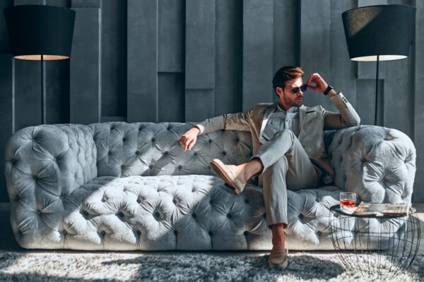 Handsome stylish man in beige suit at home sitting on sofa.