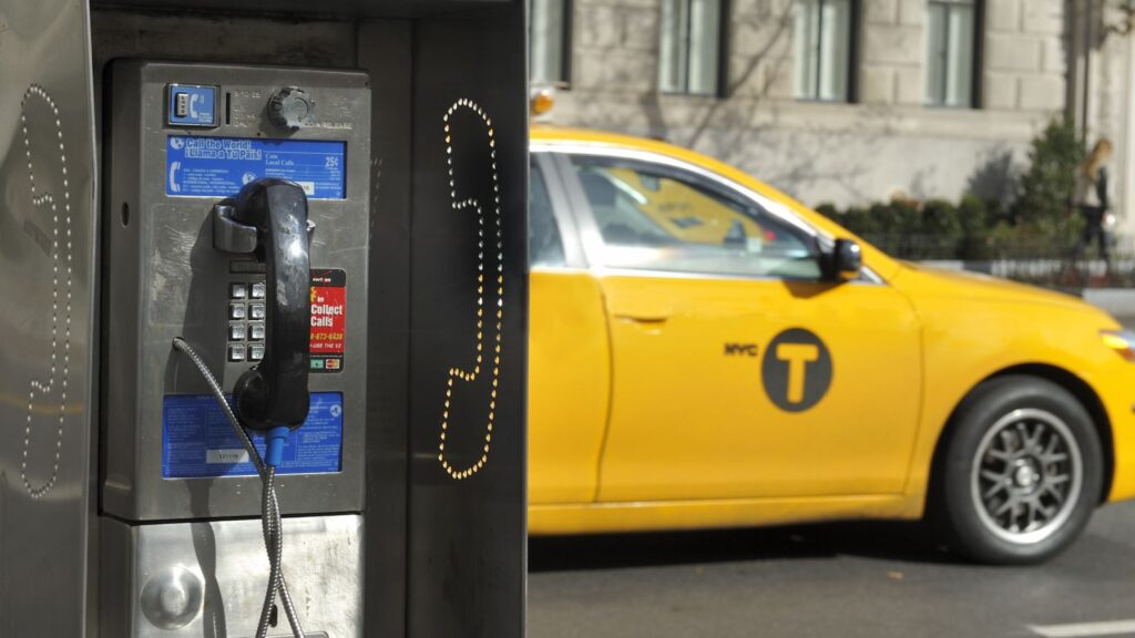 NEW YORK CITY, NEW YORK, USA - NOVEMBER 15, 2012: Old fashioned pay phone on a New York City street with a taxi passing by.November 15, 2012,New York