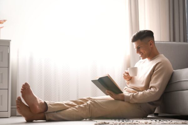 Man with cup of hot drink reading book at home. Floor heating concept