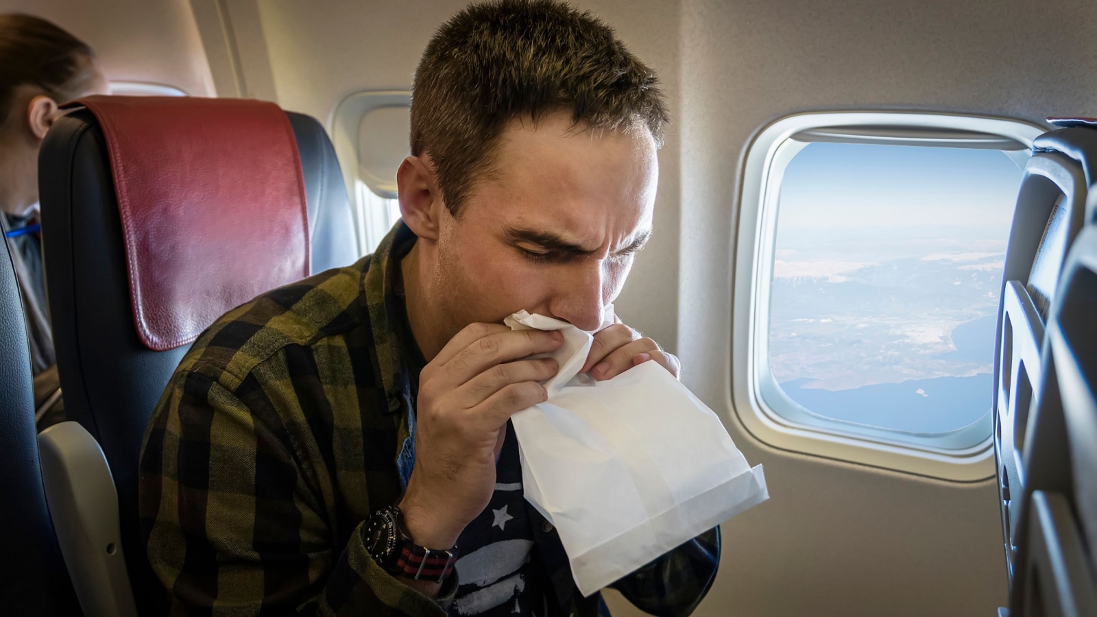 Nausea during the flight. A young guy gets carsick in transport. Nervous young man with aviophobia breathing into paper bag in airplane