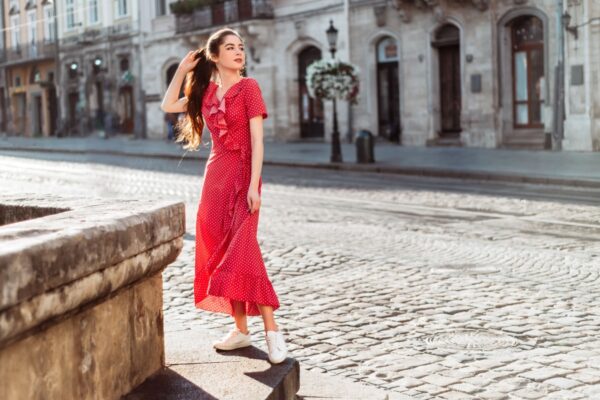 Brunette girl in red polka dot dress. Summertime woman portrait in retro outfit on old city background