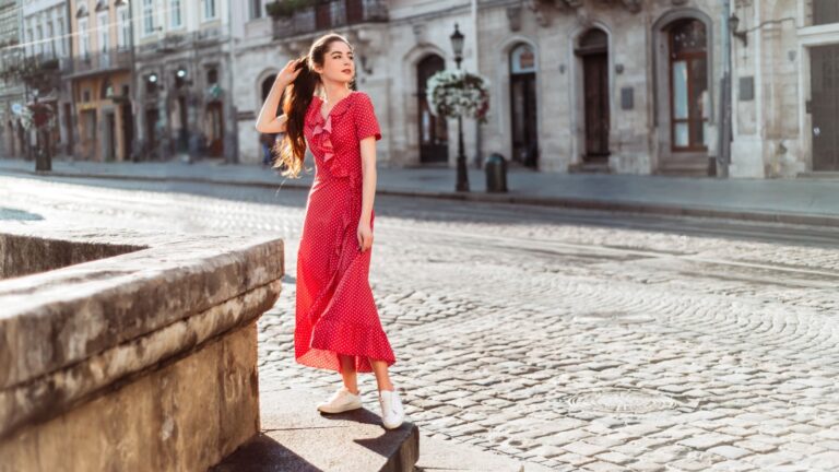 Brunette girl in red polka dot dress. Summertime woman portrait in retro outfit on old city background