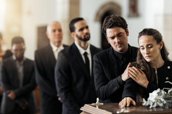 Death, funeral and family touching coffin in a church, sad and unhappy while gathering to say farewell. Church service casket and sad man and woman looking upset while greeting, goodbye and rip