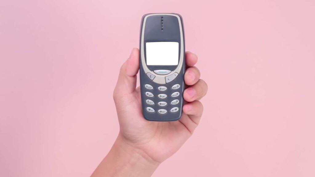 Close up hand holding mobile phone Nokia 3310 isolated on pink background. Female hand holding old used phone Nokia 3310.