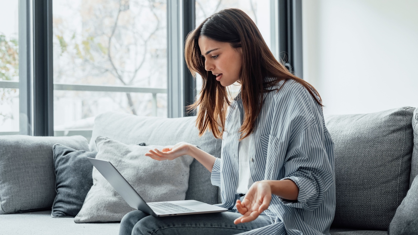 Angry young woman sit on sofa in living room frustrated having operational problems working on laptop, mad millennial girl feel stressed confused with slow internet connection or computer spam