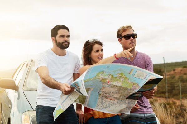 Group, reading map and travel on road trip, vacation and planning holiday for navigation by car transport. Friends, people and direction guide for journey, adventure and pointing to location outdoor