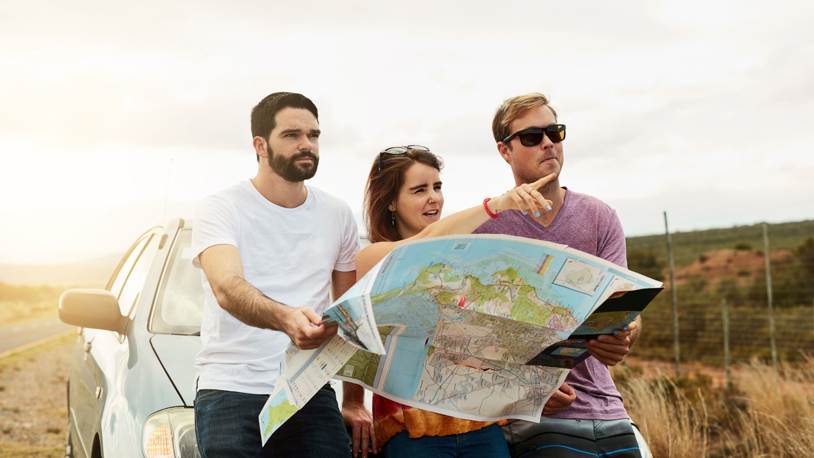 Group, reading map and travel on road trip, vacation and planning holiday for navigation by car transport. Friends, people and direction guide for journey, adventure and pointing to location outdoor