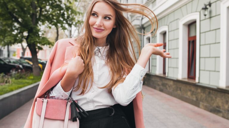 young beautiful stylish woman walking in pink coat, holding purse in hands, smiling, happy, street style, spring summer trend, black skirt, white shirt, flirty