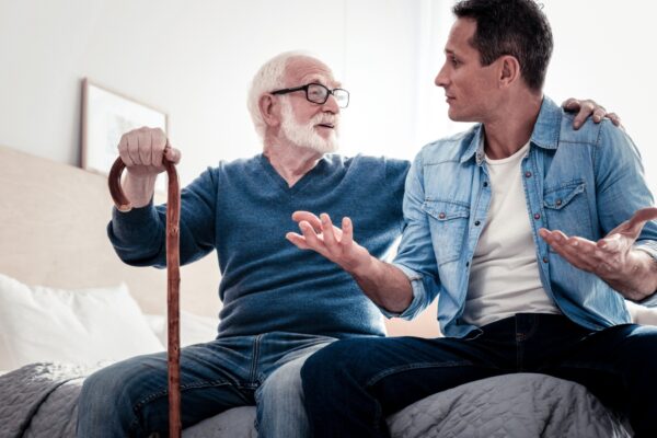 Pleasant communication. Pleasant nice elderly man looking at his grandson and holding his shoulder while talking to him