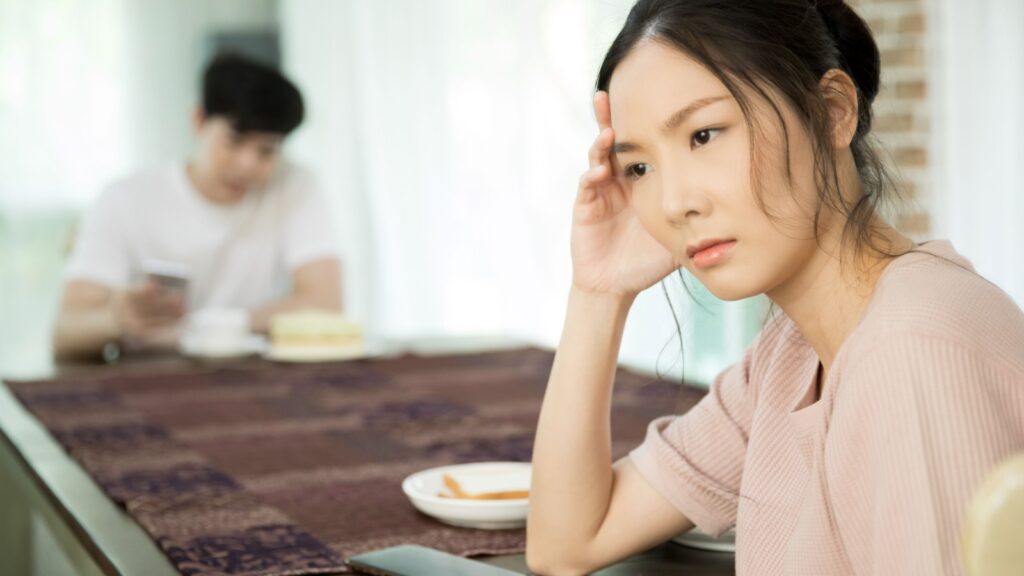 Unhappy woman sitting at dinning table keeping distance from her husband