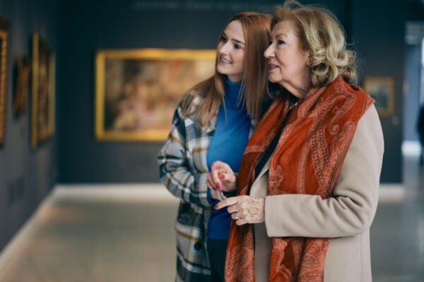 Grandmother and adolescent granddaughter are looking at the paintings in the art gallery.