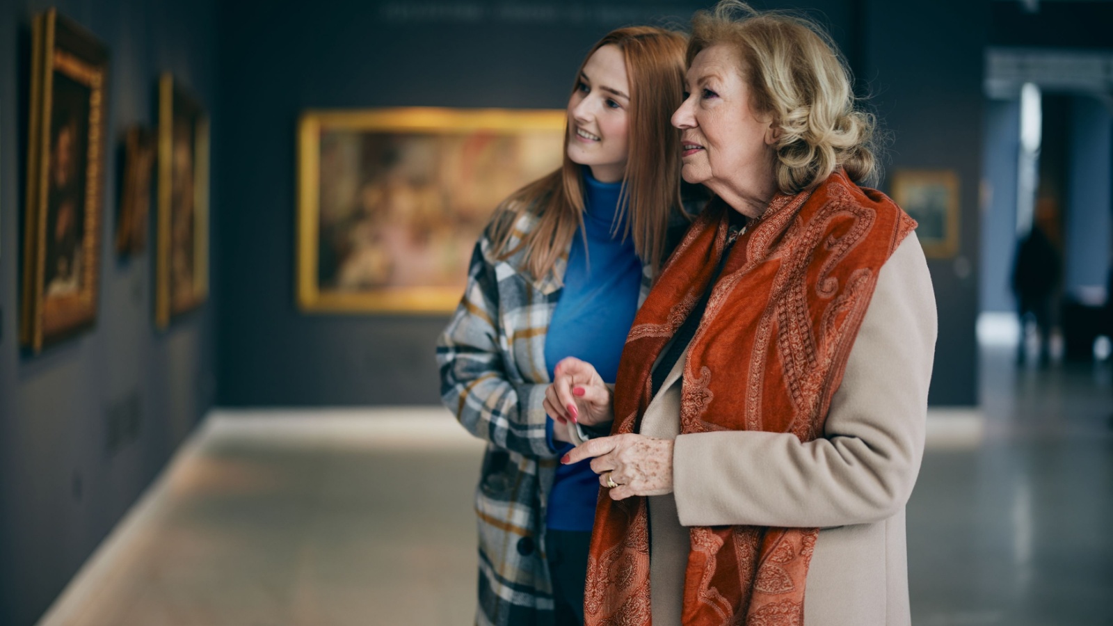 Grandmother and adolescent granddaughter are looking at the paintings in the art gallery.