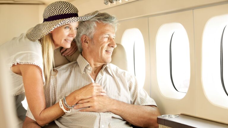 Taking a luxury trip. Smiling senior couple on an airplane looking out the window.