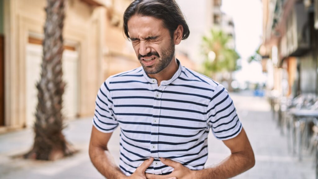 Young hispanic man with beard outdoors at the city with hand on stomach because indigestion, painful illness feeling unwell. ache concept.