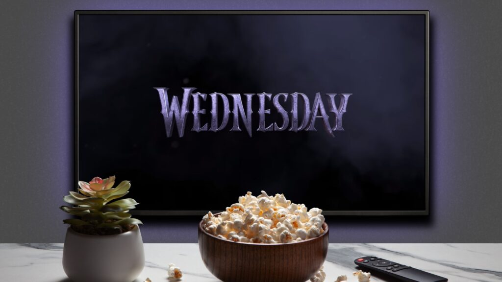 TV screen playing Wednesday trailer or movie. TV with remote control, popcorn bowl and home plant. Moscow, Russia - December 5, 2022.