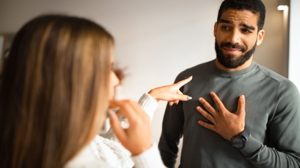 Married international millennial couple quarreling, wife pointing finger at husband in living room interior. Accusations, scandal, problems in relationships and love at home, stress